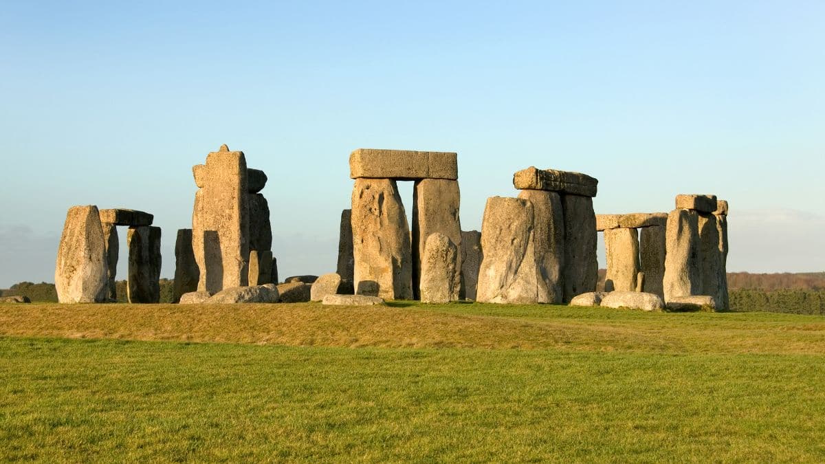 Panoramic view of Stonehenge stone circle at sunset with a clear blue sky and green grass field.