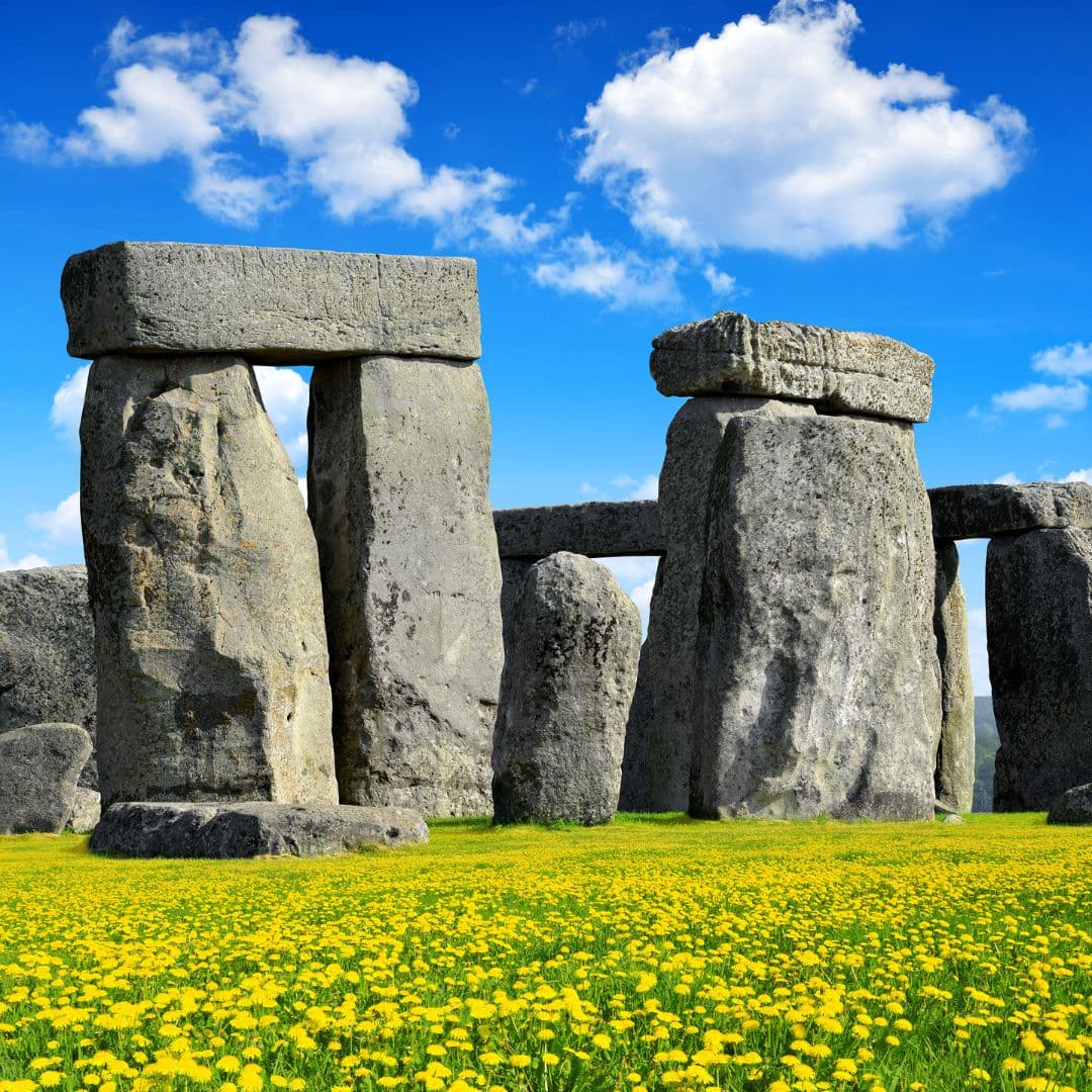 Stonehenge standing stones and lintels in low sun, with green grass in the foreground.