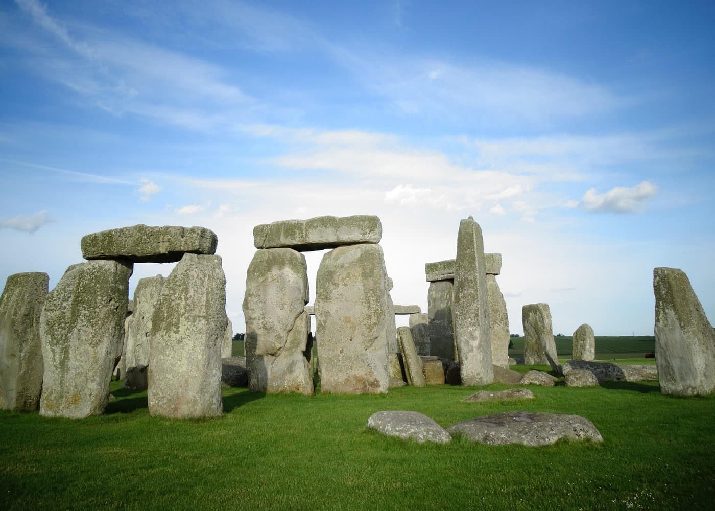 Stonehenge trilithons on a green field under a bright blue sky with thin clouds.