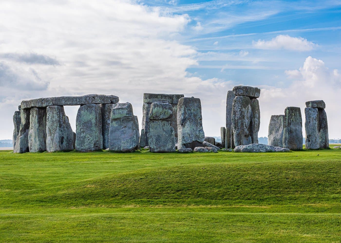 Wide view of the Stonehenge circle on Salisbury Plain under a blue sky with white clouds.