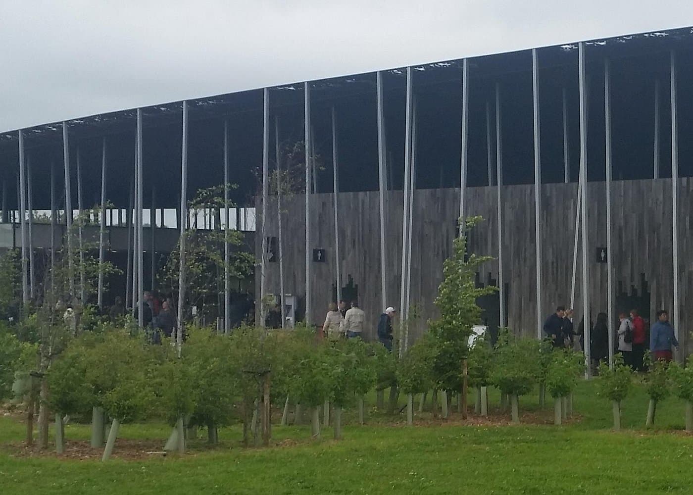 The Stonehenge Visitor Centre canopy on steel pillars, with visitors on the grass in front.