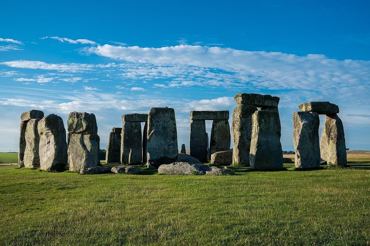 Stonehenge on a bright day with green grass and a blue sky behind the sarsen stones.