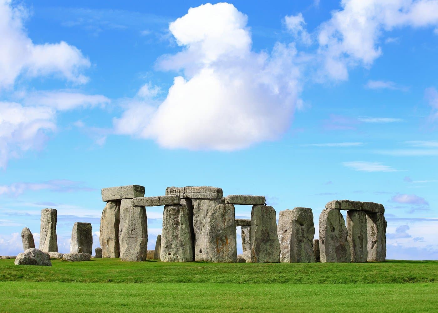 Stonehenge trilithons on a sunny afternoon with a blue sky and a band of cloud behind the stones.