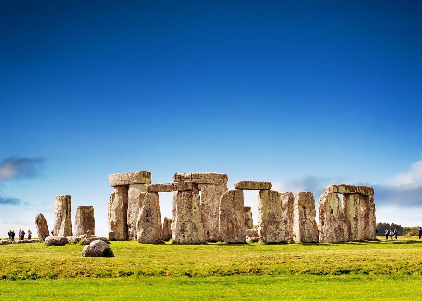 Wide view of Stonehenge on a bright day with visitors walking around the stone circle.
