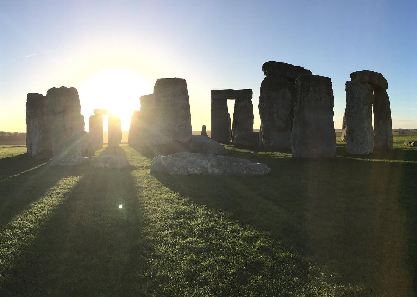 Stonehenge at sunrise, the stones silhouetted with long shadows on the grass.