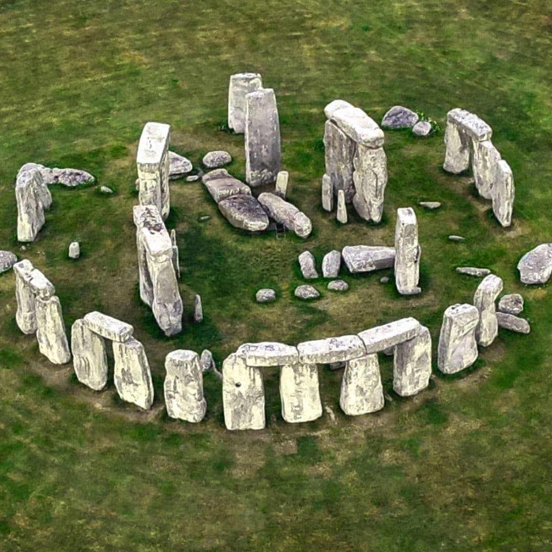 Three standing stones and lintels at Stonehenge with birds on the grass in the foreground